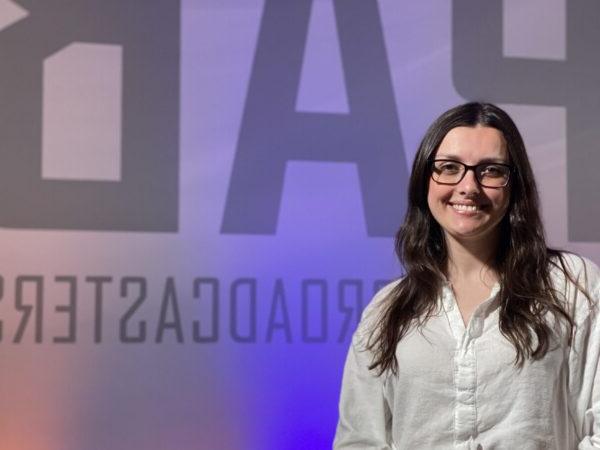 Image shows Makenzie Christman holding her PAB Award in front of a wall that says, "PAB."